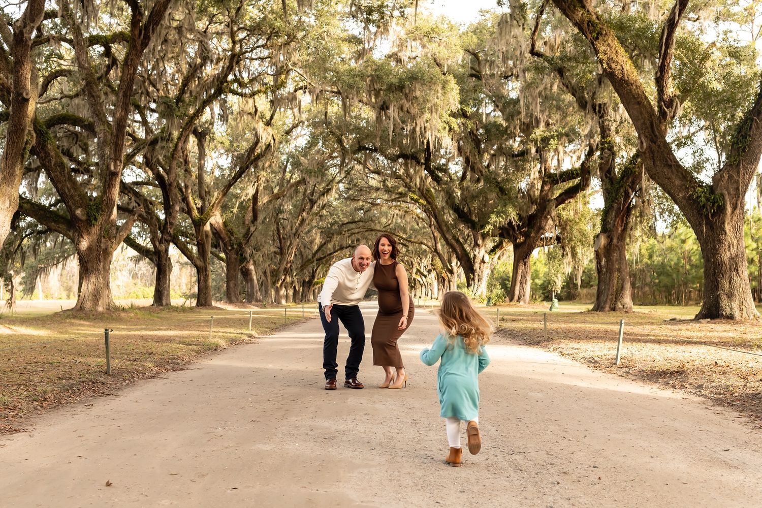 Young child runs joyfully ahead on a path lined with majestic Spanish moss-draped oak trees during golden hour.