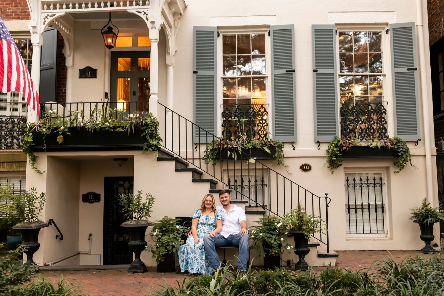 A couple relaxes on the steps of a historic Charleston-style home with blue shutters and ornate architecture on Jones Street in Savannah.