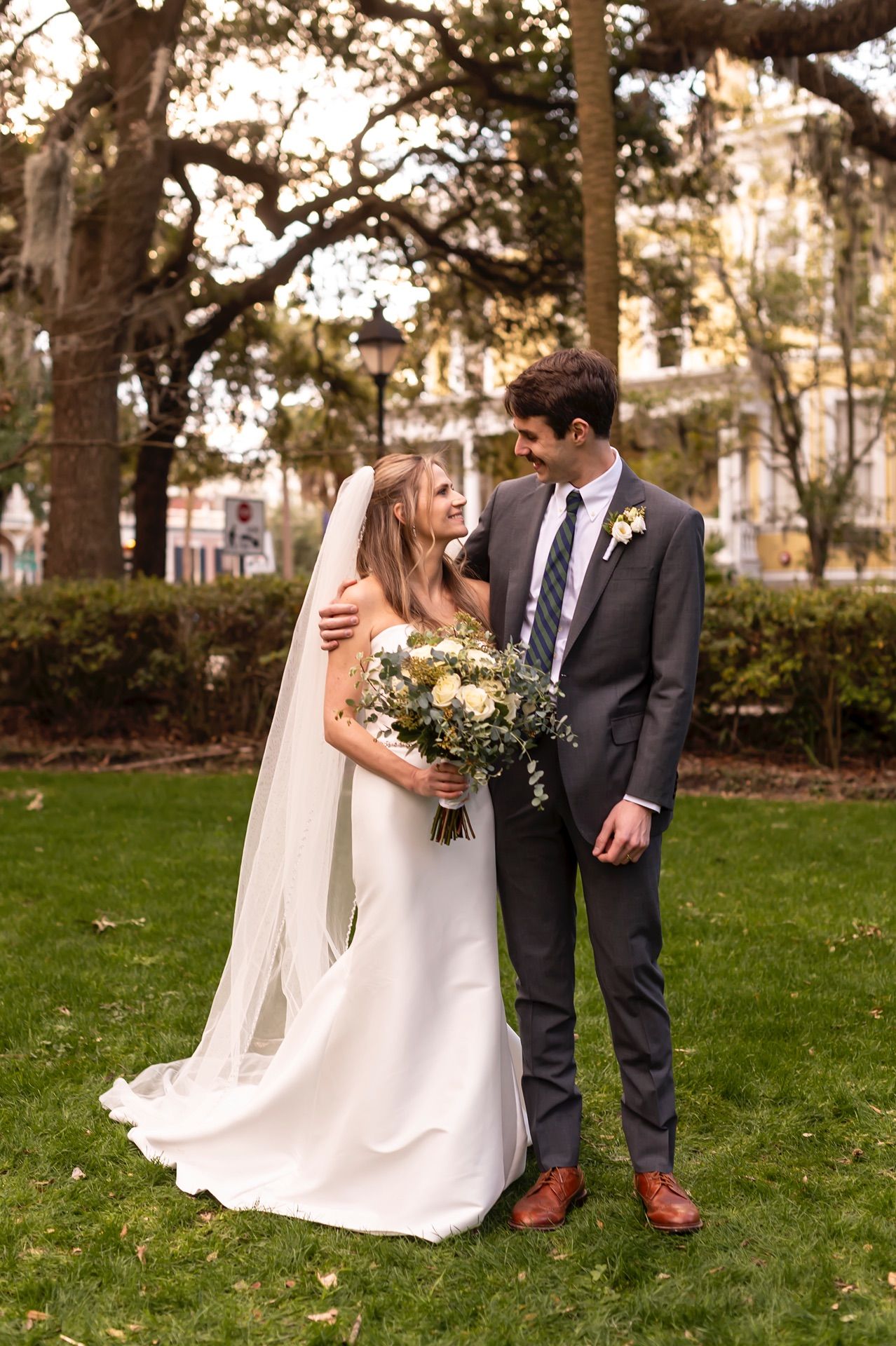 Couple in wedding attire poses on green lawn in series of romantic shots under autumn trees.