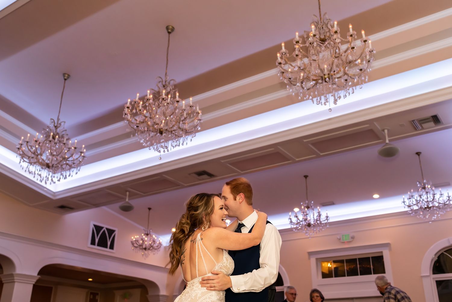 A couple shares a romantic dance under elegant crystal chandeliers in a grand ballroom setting.