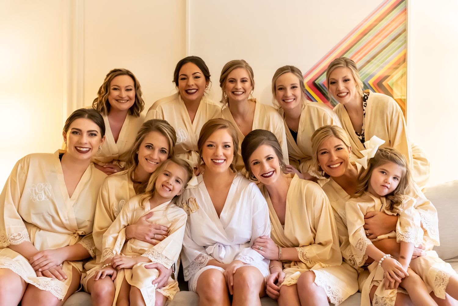 A bridal party wearing matching robes sits on stairs together smiling for a pre-wedding photo.