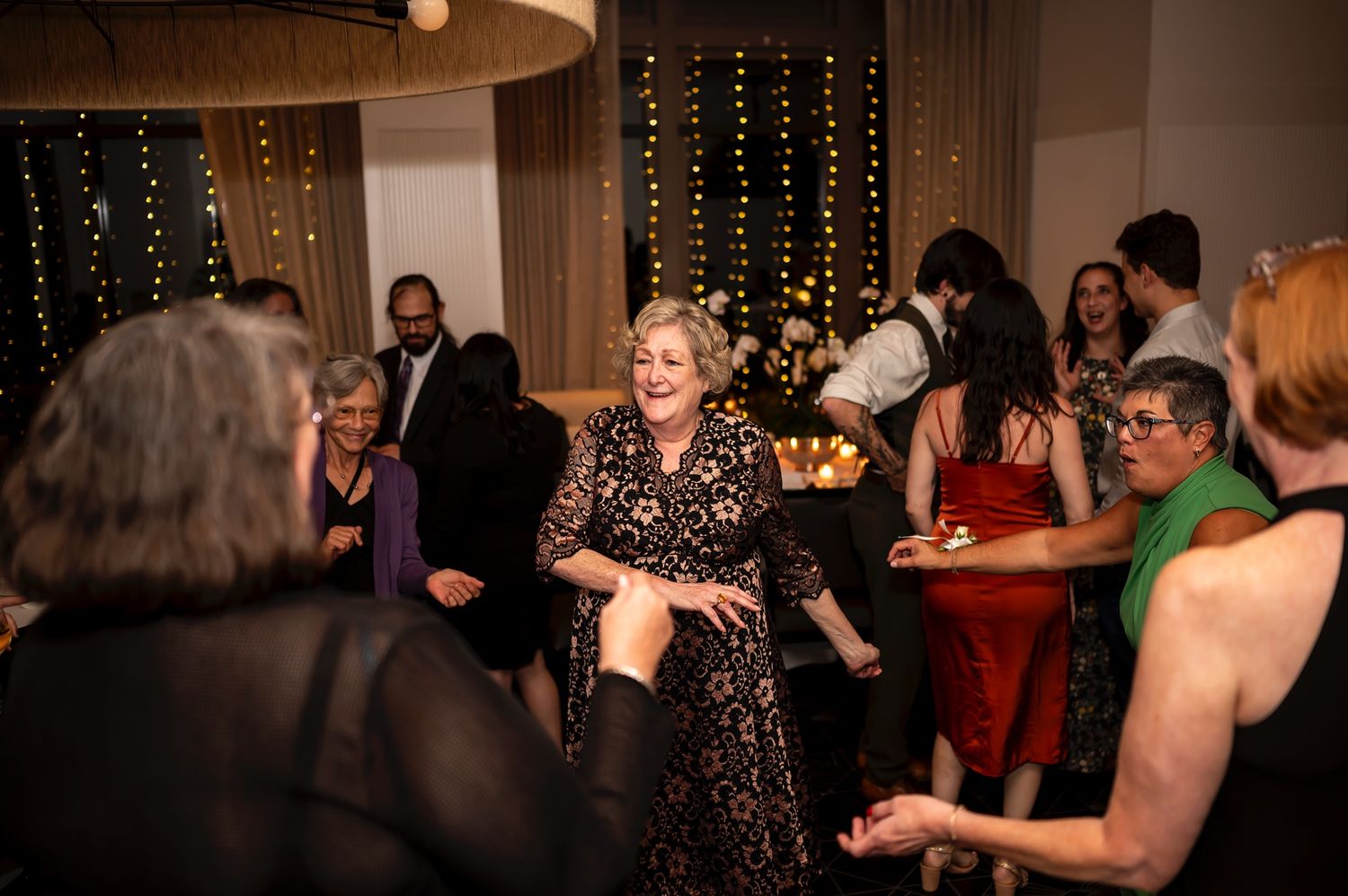 People dancing and enjoying themselves at a celebration with glowing string lights decoration in the background.