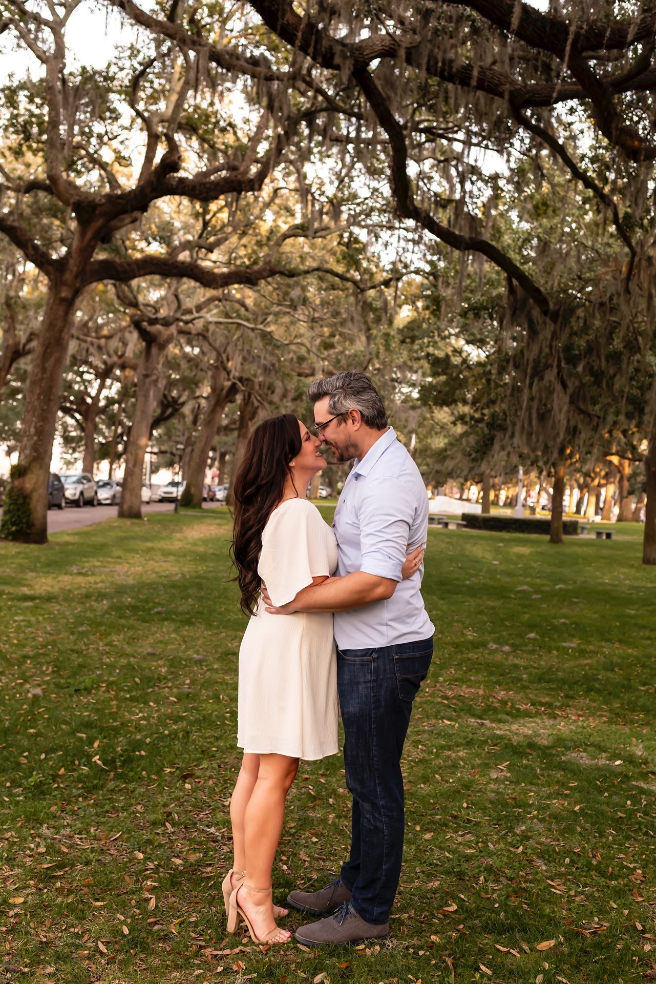 A couple embraces beneath Spanish moss-draped oak trees during golden hour in a romantic Southern park setting.