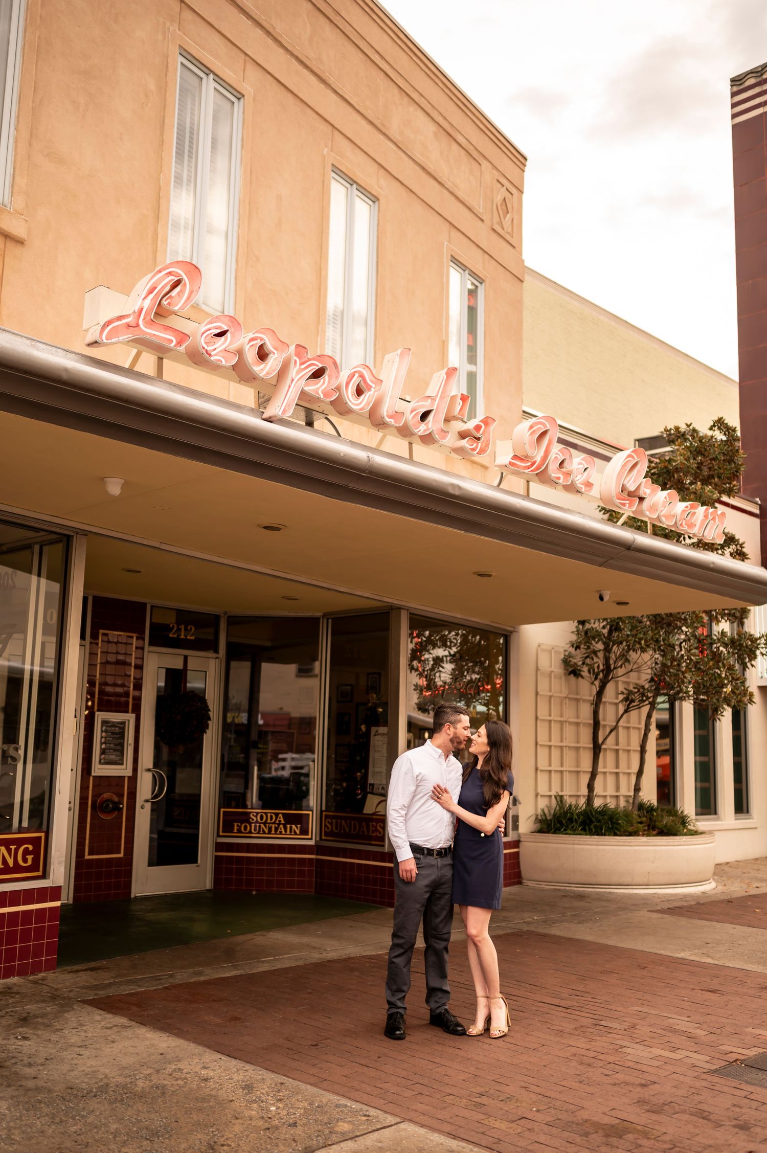 A couple stands outside a vintage theater with retro signage and art deco architecture during sunset.