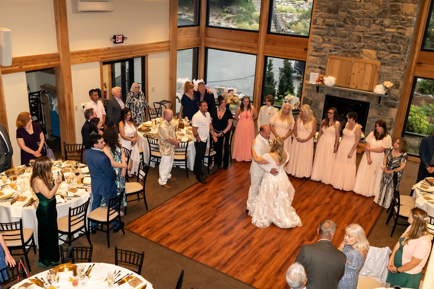 Wedding celebration with guests gathered around a dance floor in a rustic venue with stone walls and hardwood flooring.