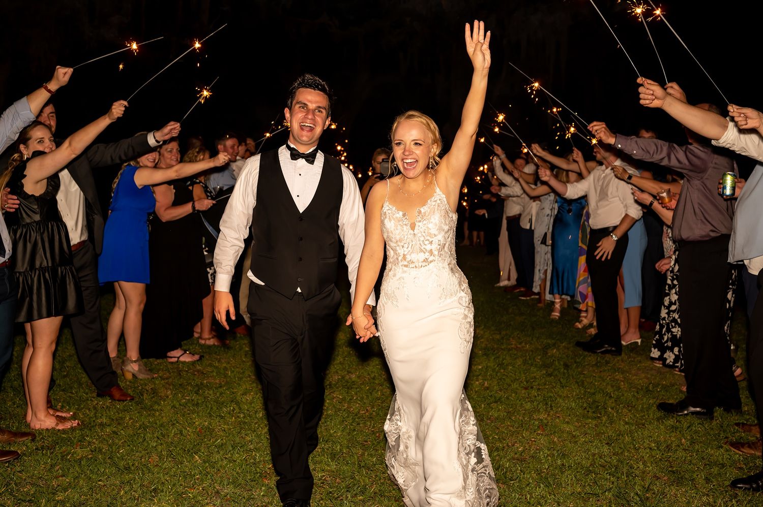 A joyous exit as newlyweds walk through their wedding guests during an evening outdoor celebration.
