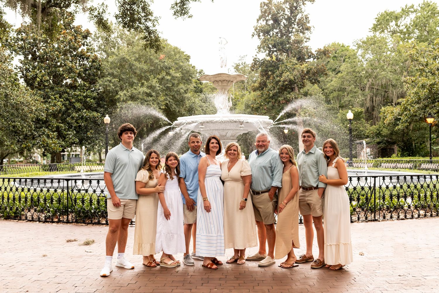 A group in coordinating neutral outfits poses together on a sandy pathway in an outdoor setting.
