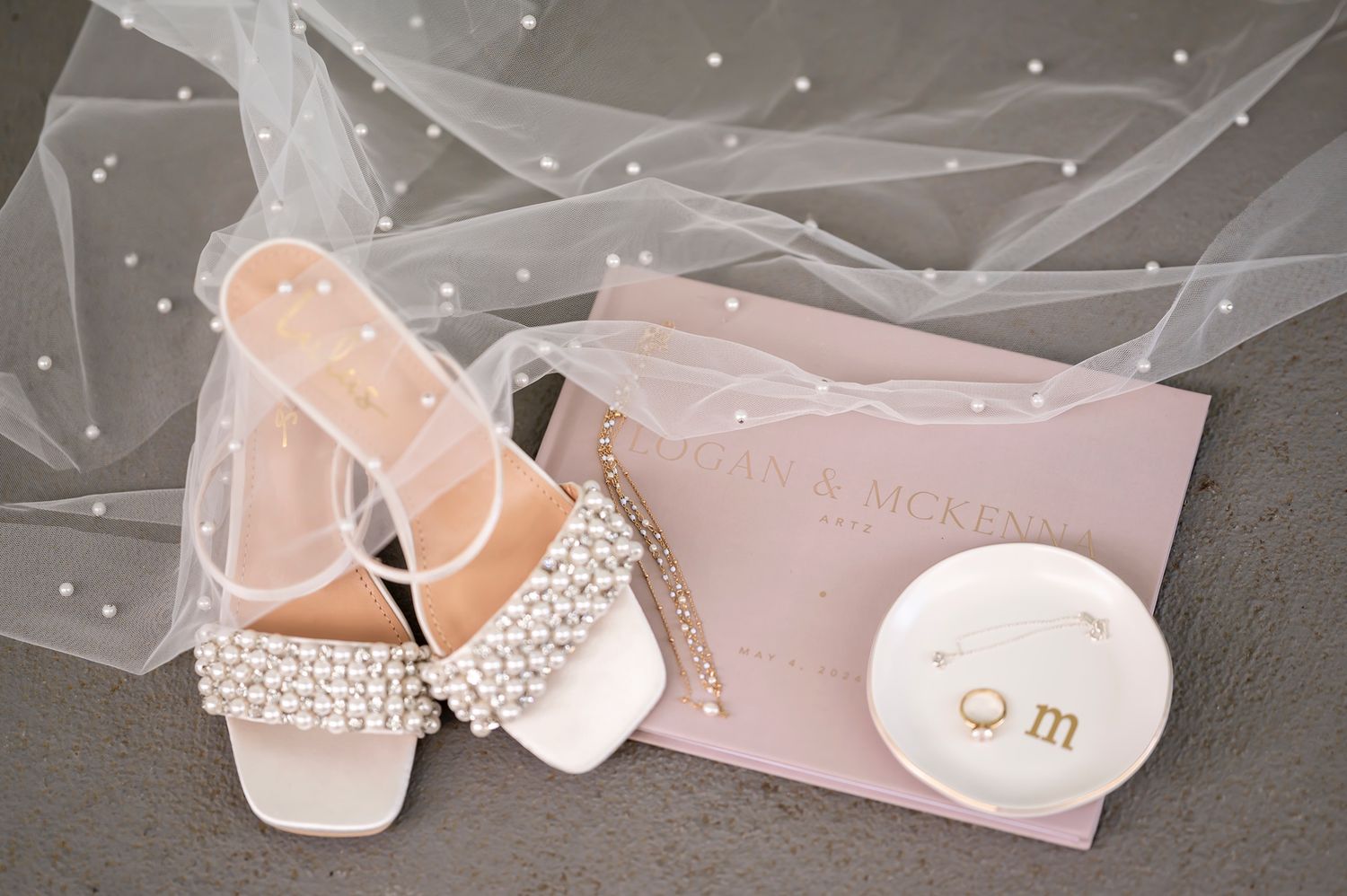 Elegant bridal shoes adorned with crystals next to a pink wedding invitation and delicate white veil.