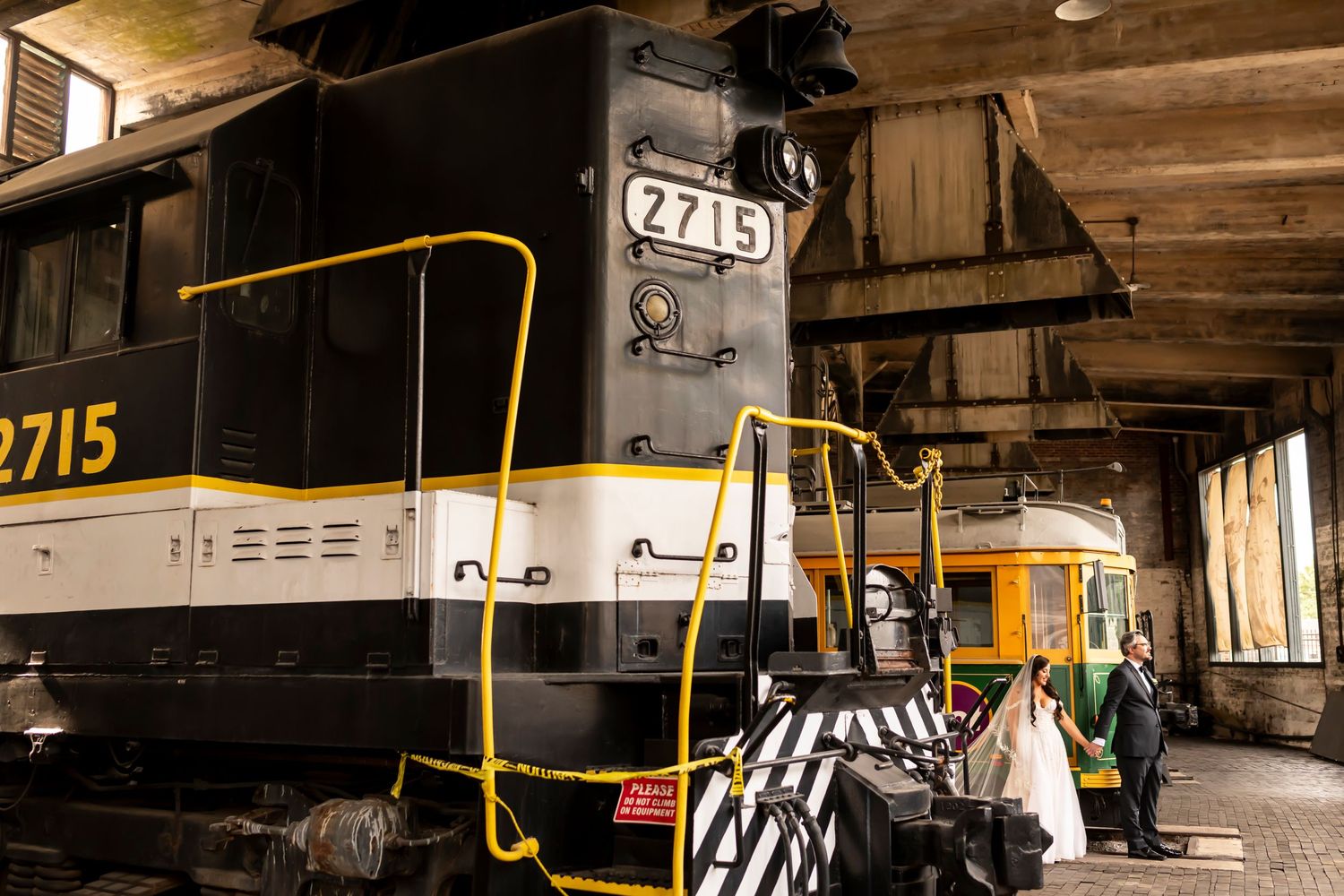 A long row of old subway train cars displayed in a historic railway museum or depot with rustic wooden beams above.