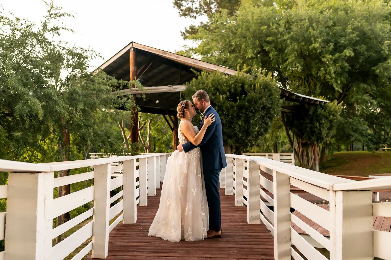 A couple shares an intimate moment on a white wooden bridge surrounded by lush greenery.