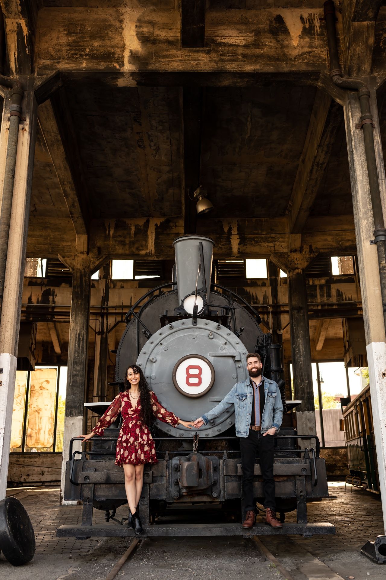 Vintage steam locomotive numbered 8 in an old train depot with a couple standing in front of it.