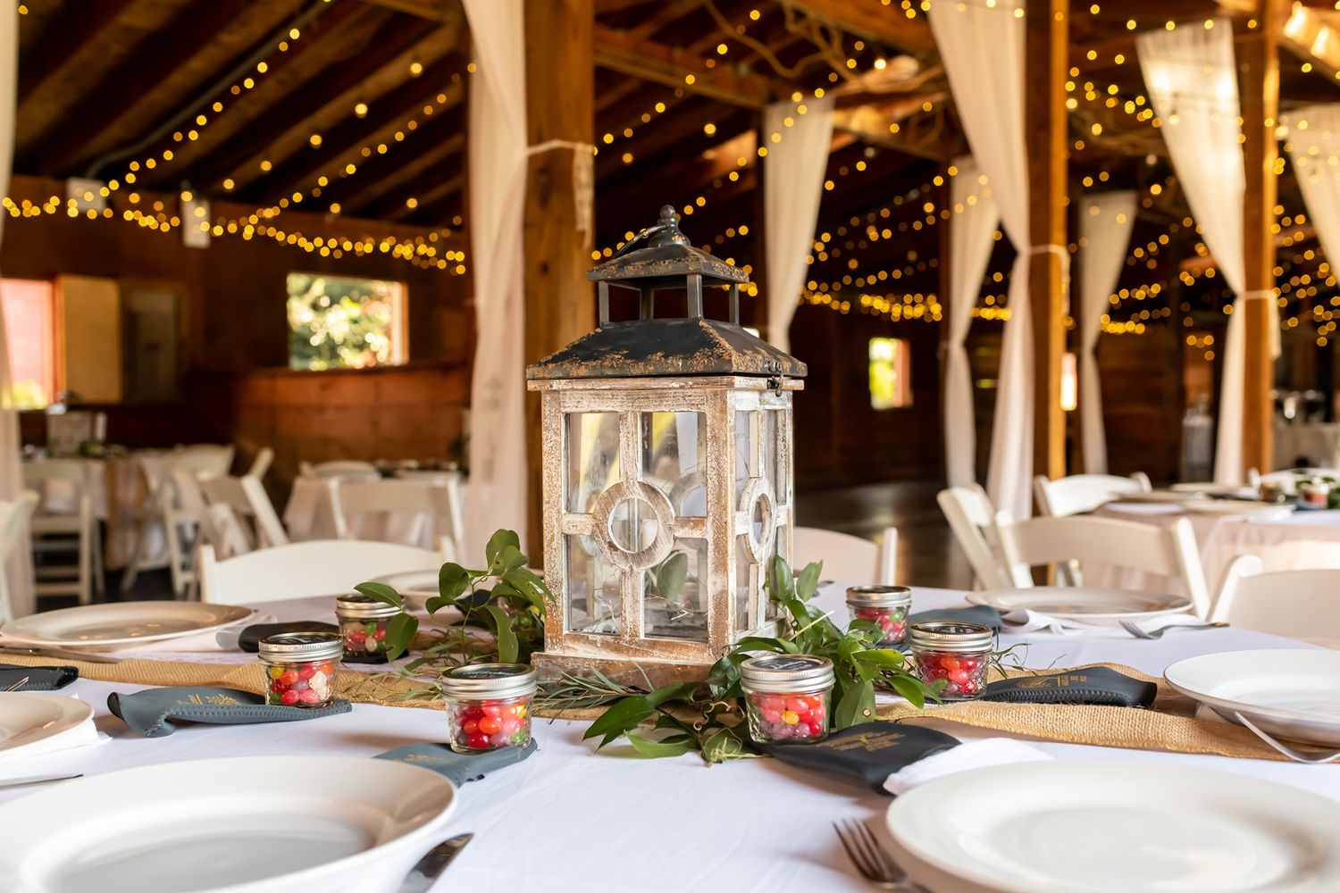 A rustic barn wedding reception venue with elegant table settings and string lights hanging from wooden beams.