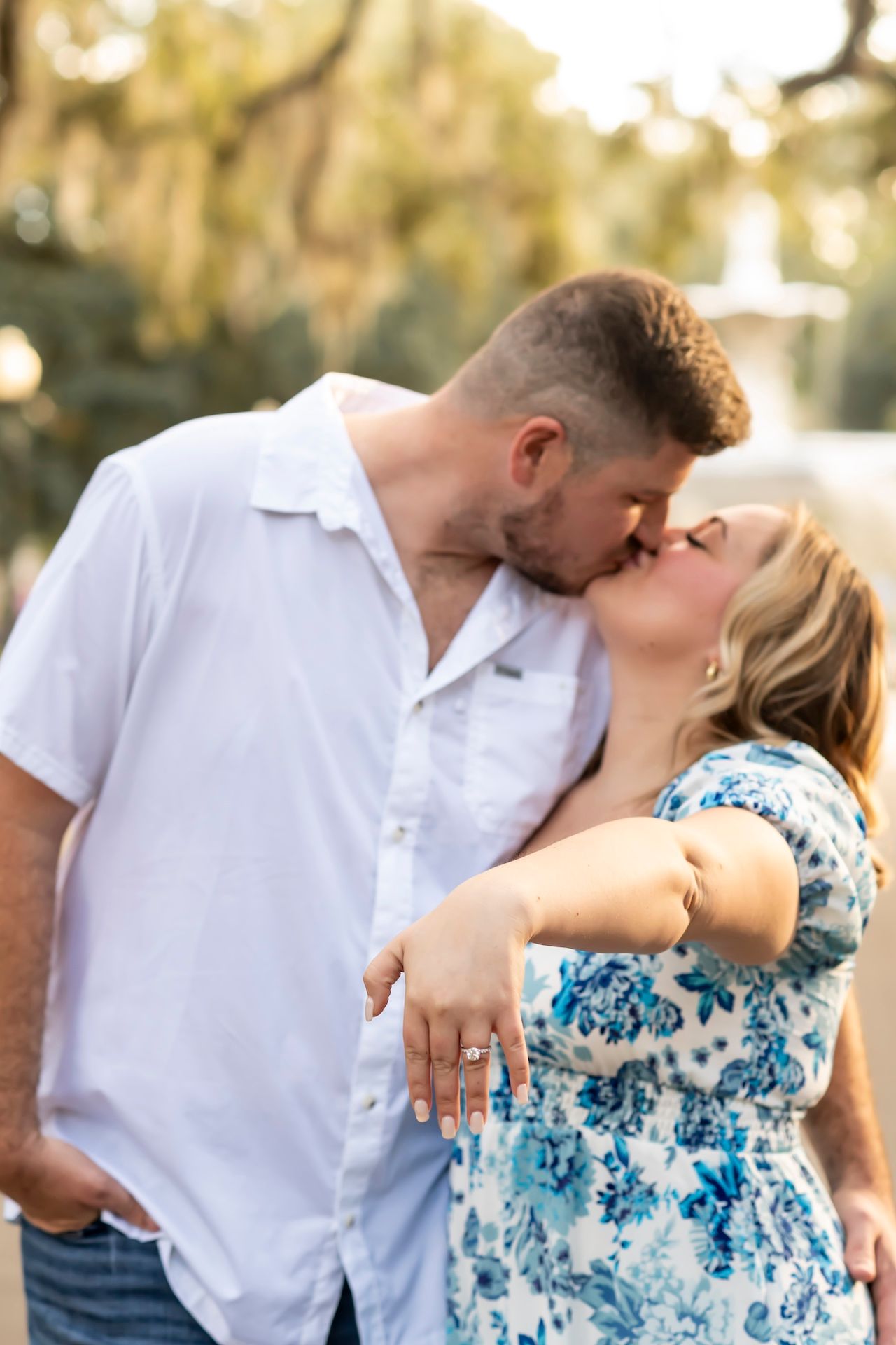 A romantic couple share an intimate kiss outdoors in a garden setting at sunset.