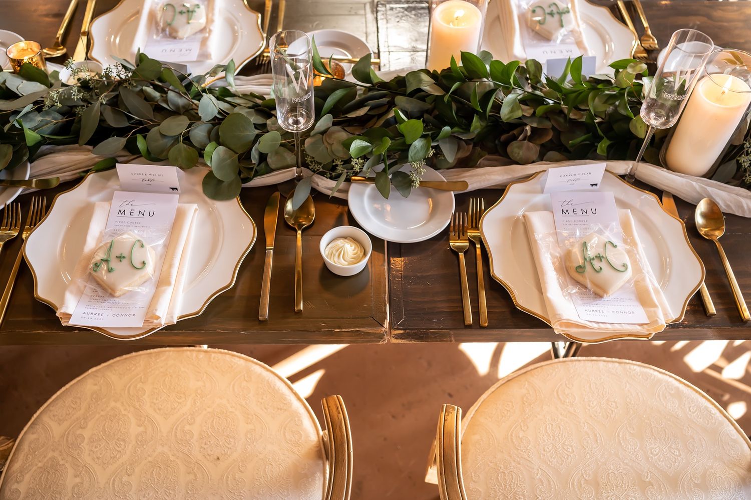 Elegant wedding reception tablescape with delicate white place settings and greenery garland decor at a rustic venue.