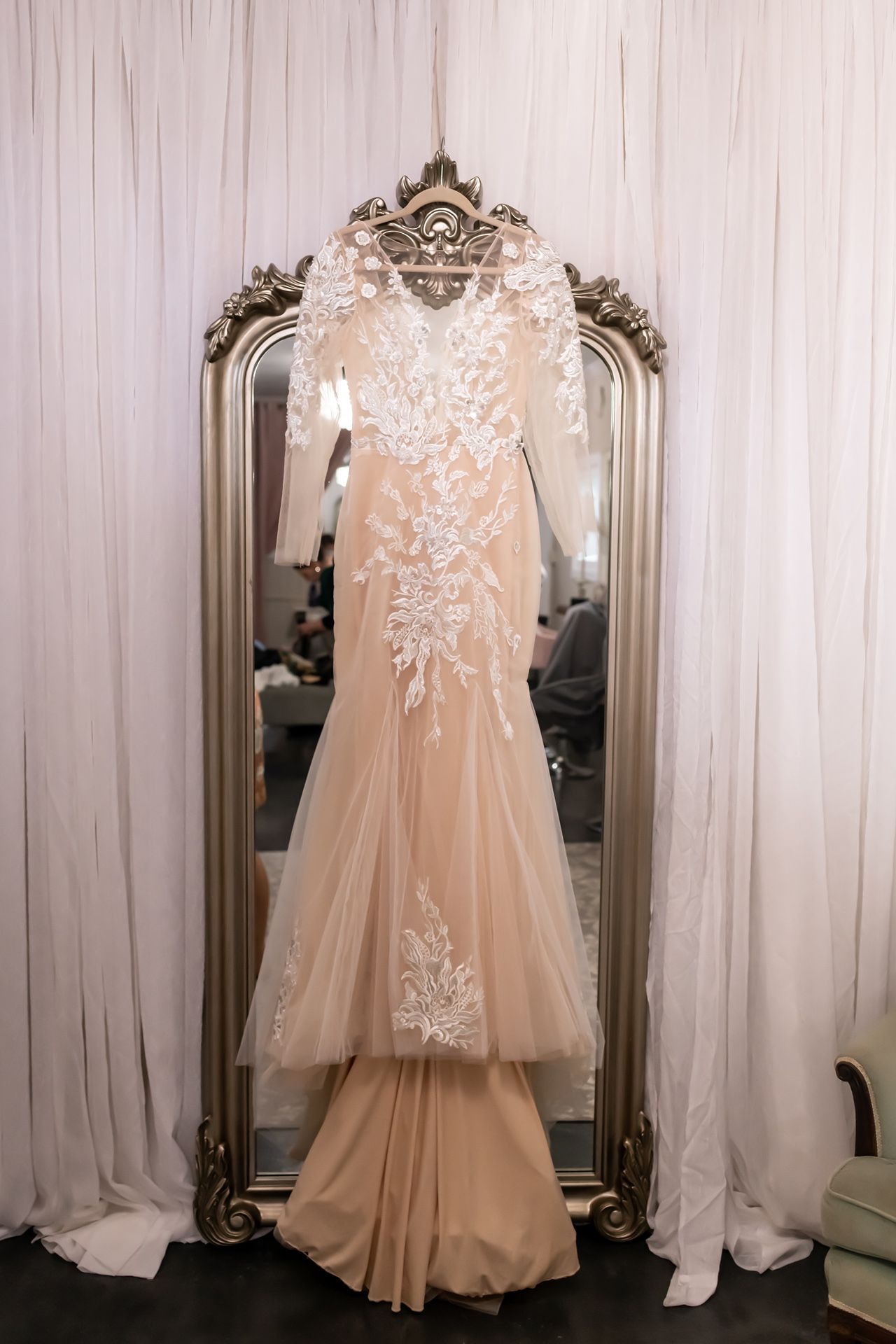 A peach-colored bridal gown with white lace appliques displayed against a white curtained background in various angles.