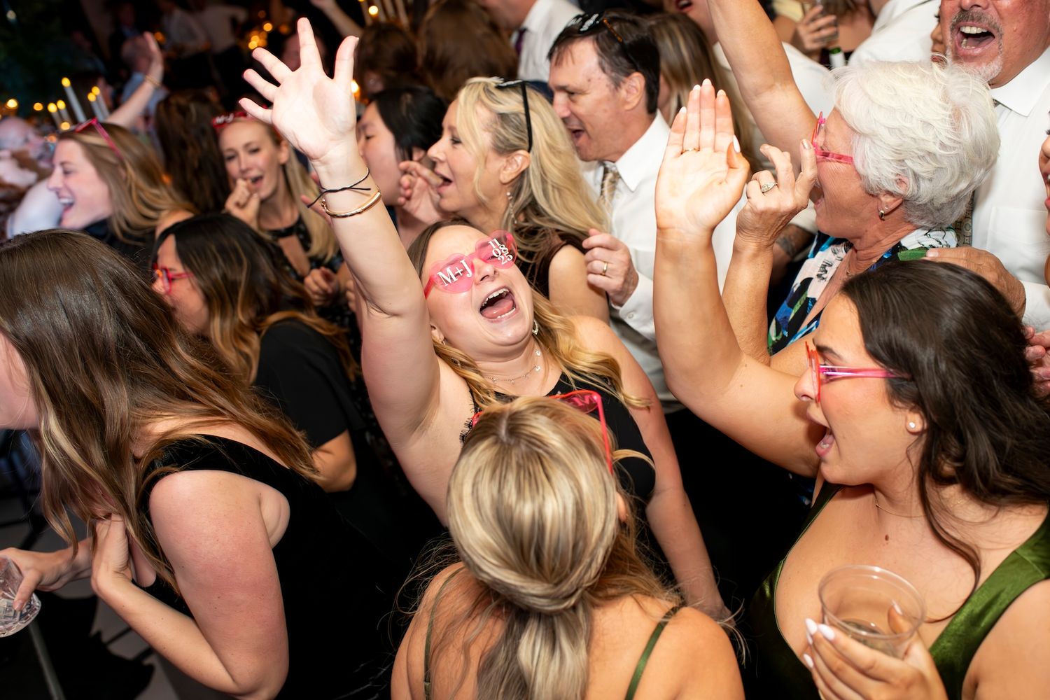 A lively crowd of people dancing and celebrating at a party with energetic expressions and raised arms.