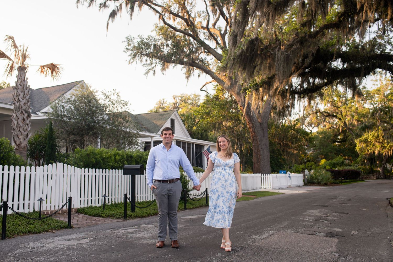 A couple walks hand in hand down a tree-lined residential street at sunset creating a romantic silhouette.