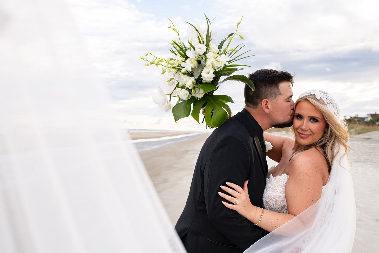 A romantic series of beach wedding photos showing a couple embracing and kissing in formal attire by the ocean.