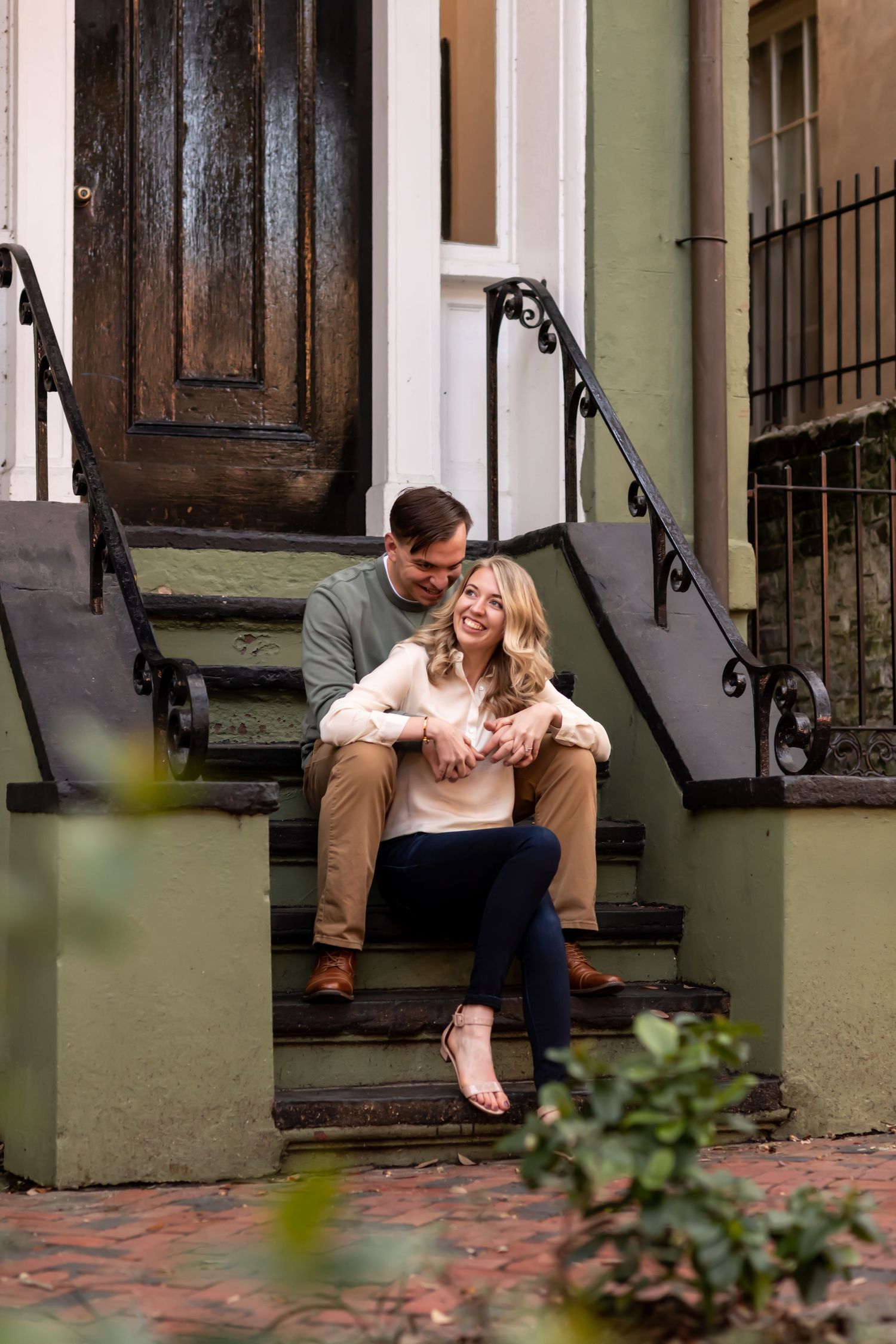 A couple sits together on concrete steps in front of a brick building with an iron railing.