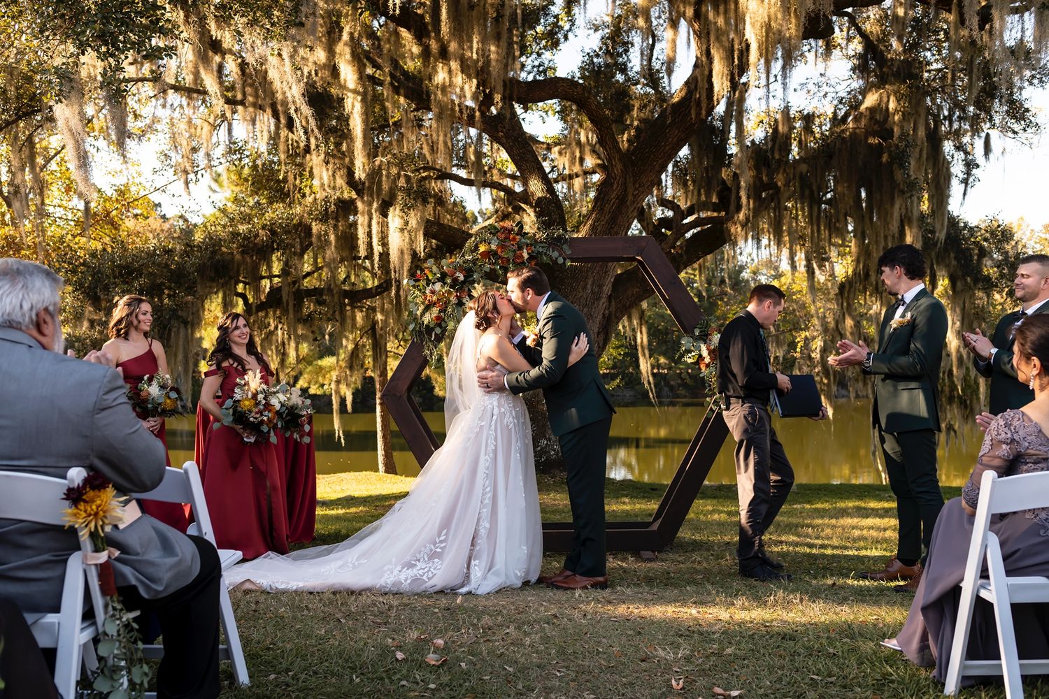 A romantic wedding ceremony takes place under Spanish moss-draped oak trees at golden hour.