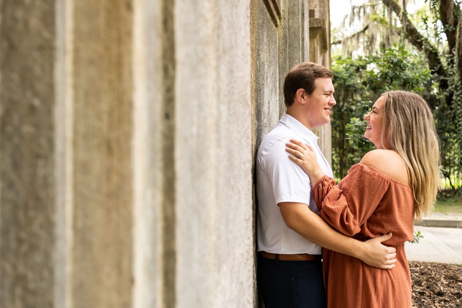 Couple in sunset lighting poses romantically against rustic stone pillars in an outdoor setting.