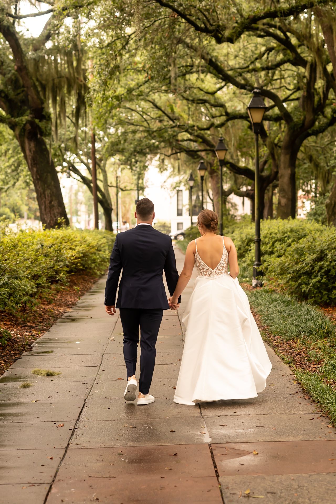 Two figures walk down a scenic tree-lined path with Spanish moss hanging from oak branches overhead.