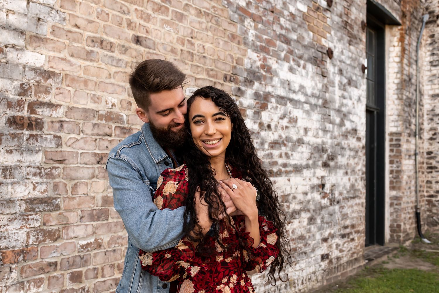 A couple embraces and laughs together against an aged brick wall background.