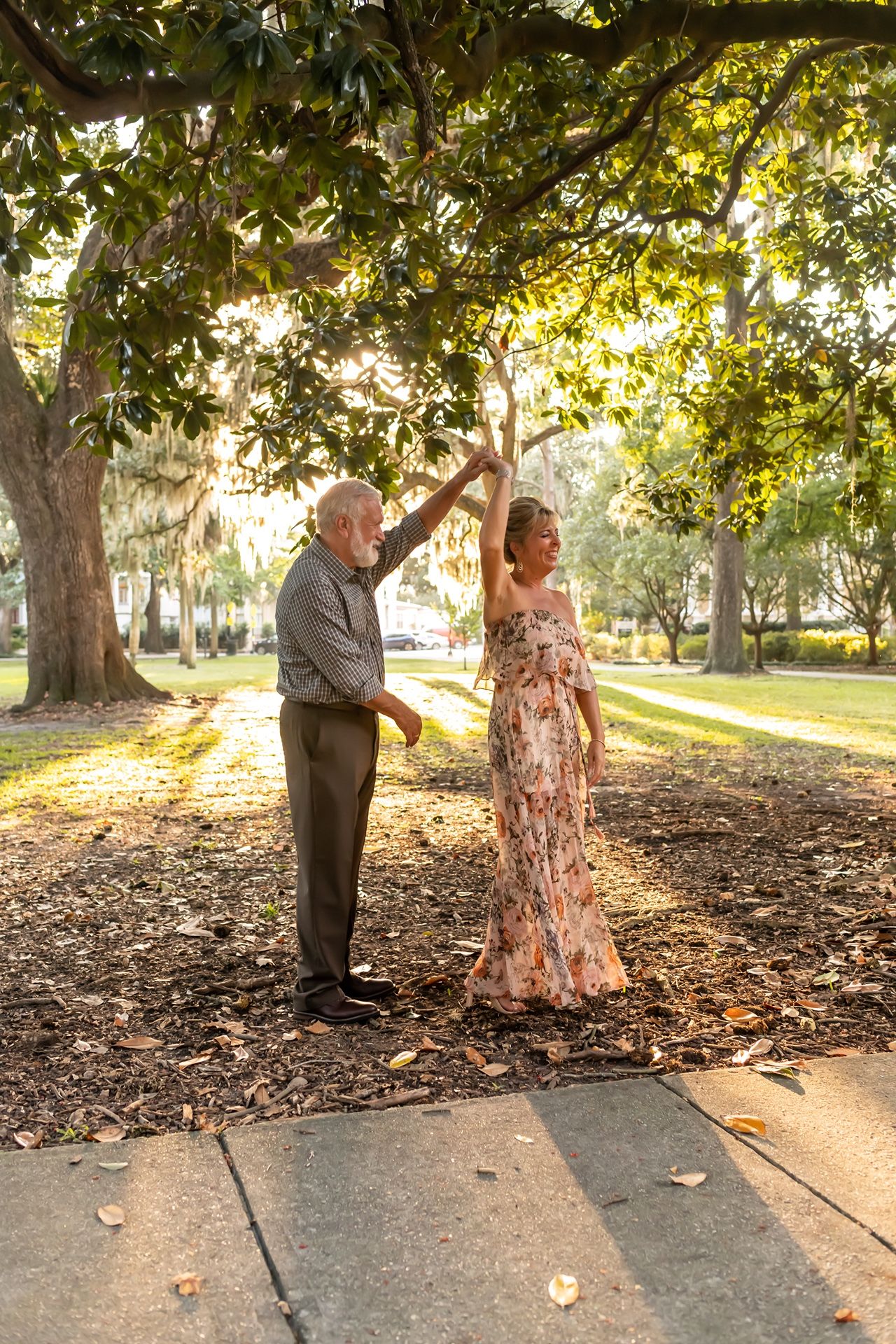 Dancing couple twirls together in a park setting among fallen leaves and dappled sunlight.
