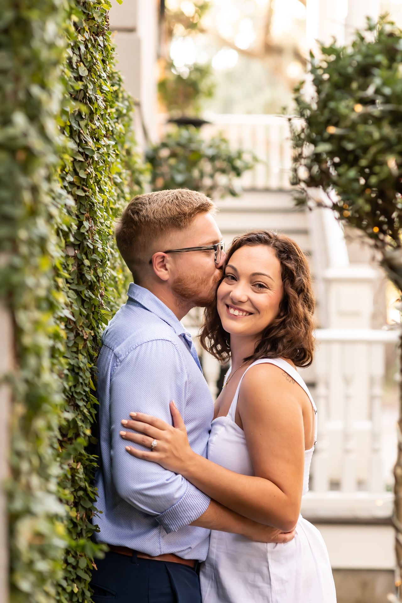 Romantic couple embraces outdoors next to ivy-covered wall in summer garden setting.