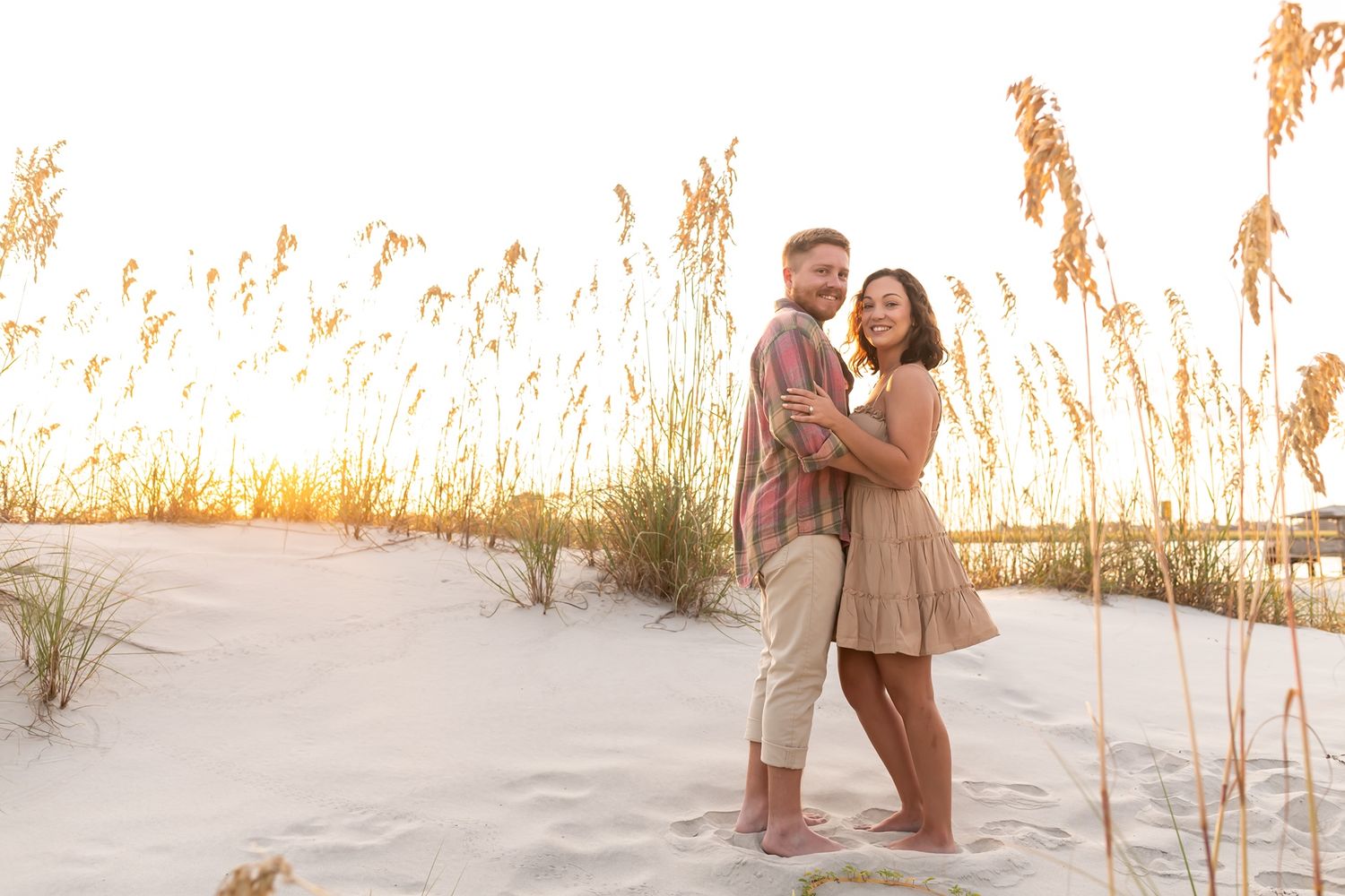 A couple walks together through tall beach grass at sunset along a sandy shoreline.