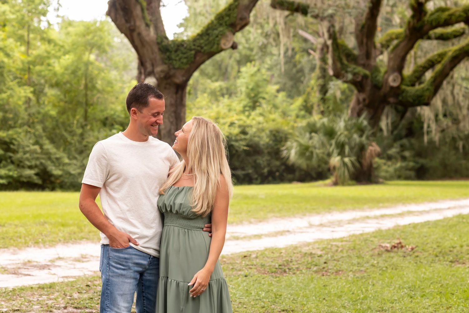 Couple sharing a romantic moment on a dirt path under moss-covered oak trees in a sunlit Southern garden.