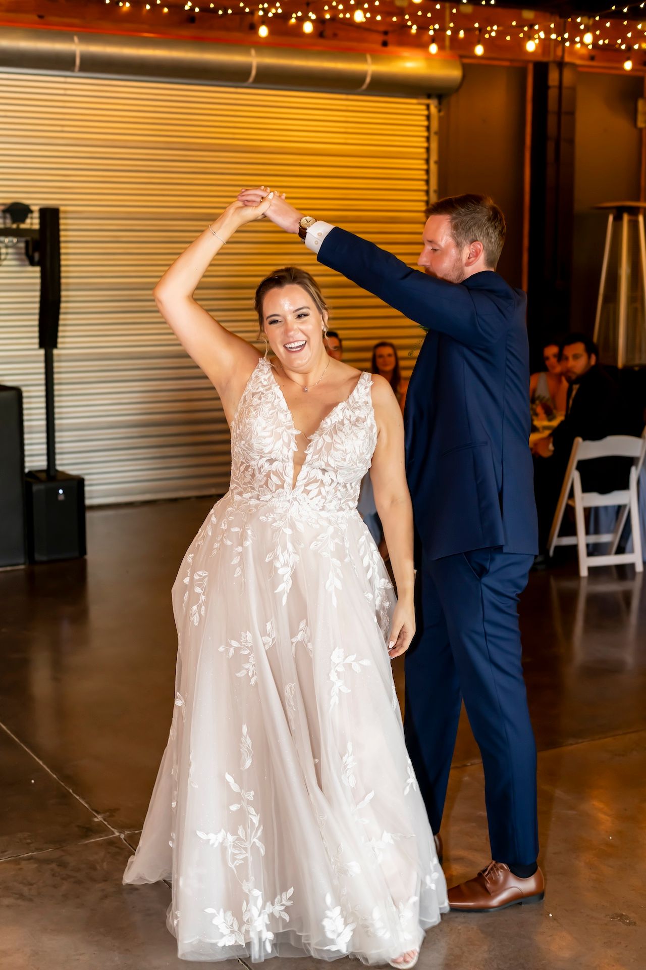 Elegantly dressed couple dancing at a wedding reception with twinkle lights overhead and a white dress spinning.