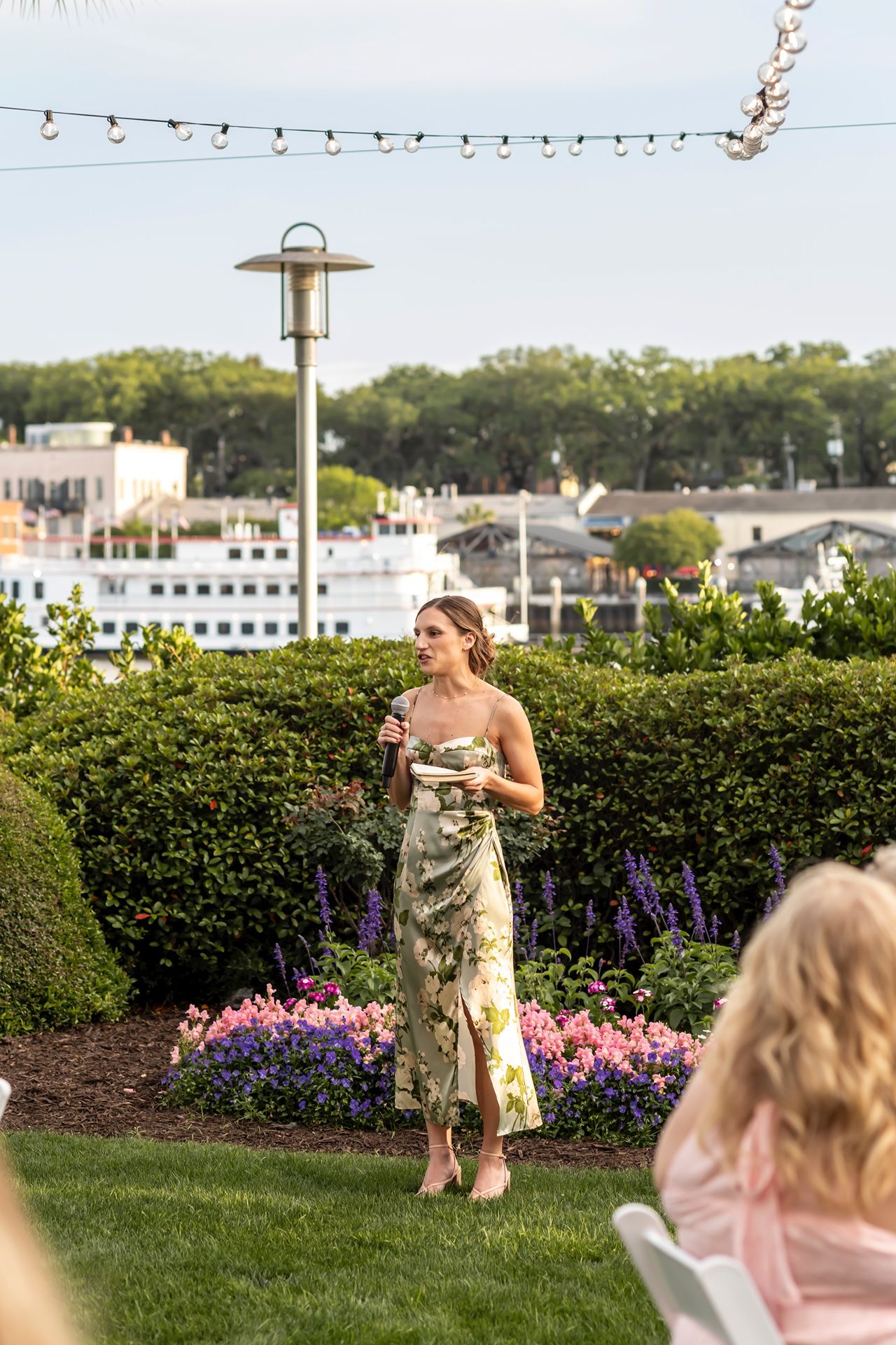 People enjoying a backyard celebration with string lights and blooming flowers in a garden setting at dusk.