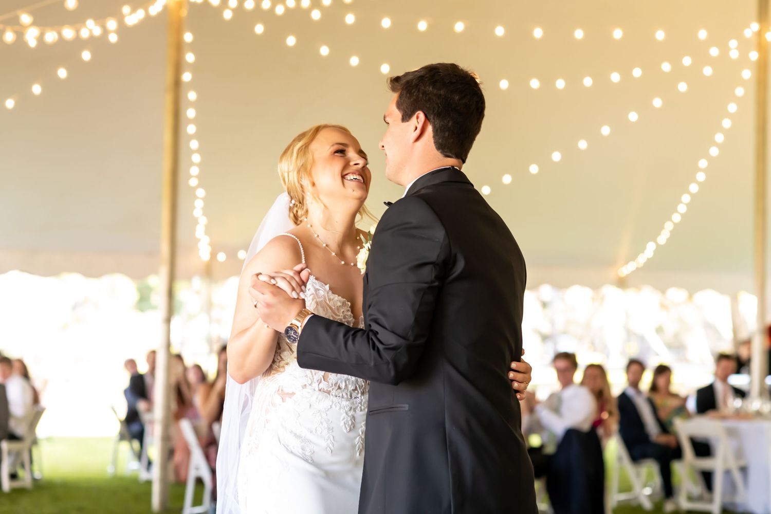 A couple shares their first dance under a tent with string lights during their wedding reception.