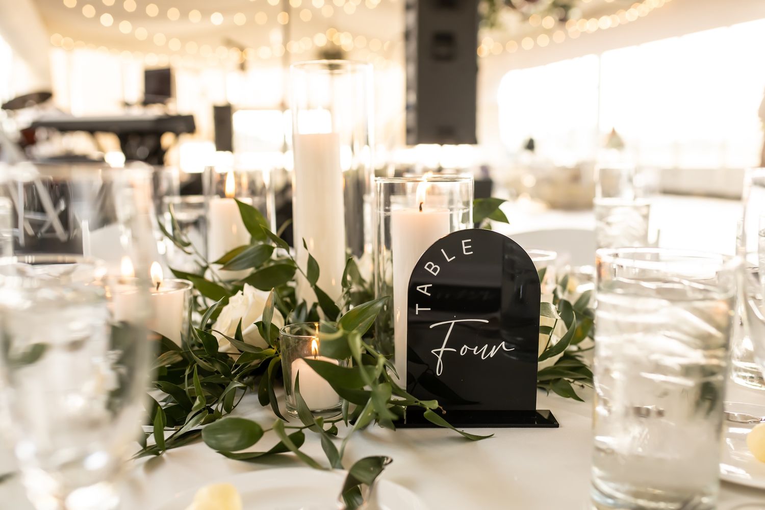 White and green wedding reception decor with glass candle holders and eucalyptus garland on tables.