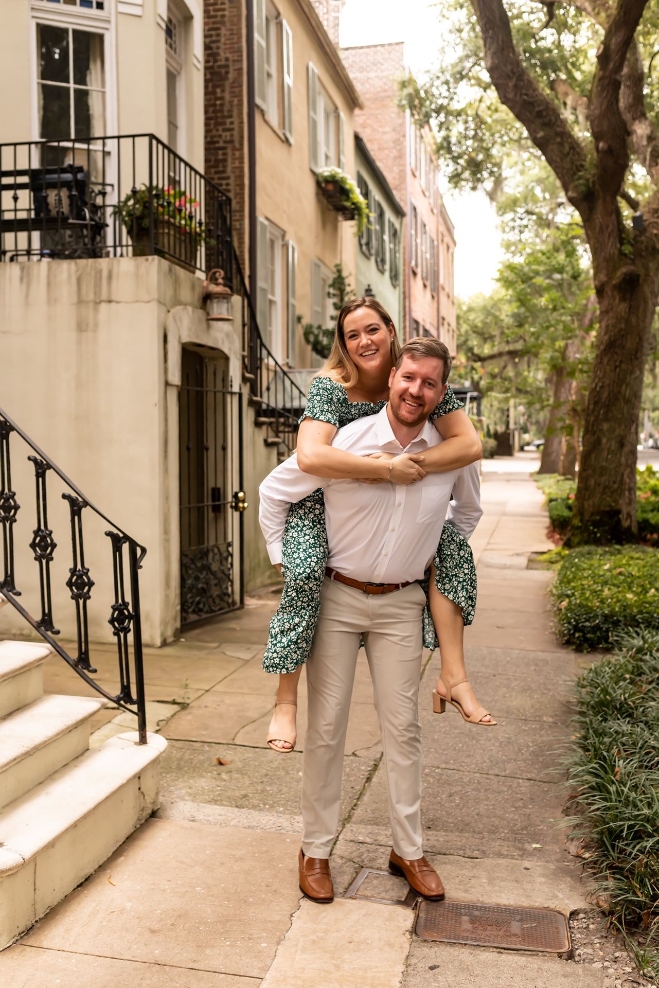 A playful couple stands together on a charming historic street lined with brick townhouses and iron railings.