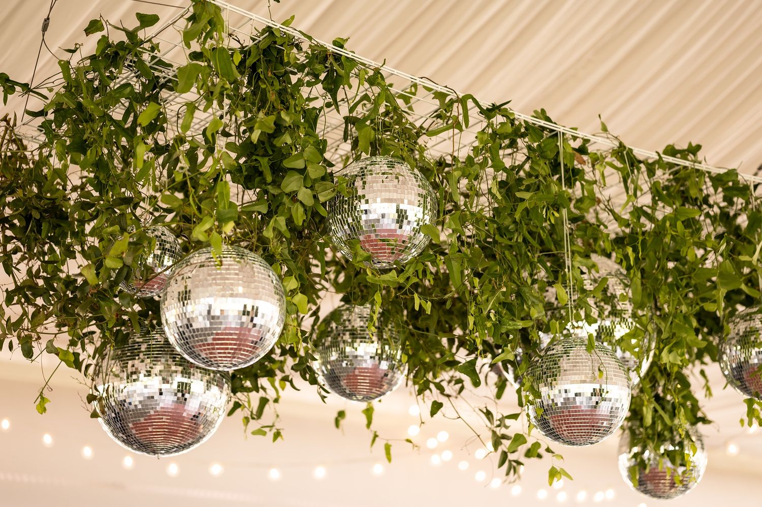Disco balls and lush green foliage decorate an elegant event venue with white draping ceiling.