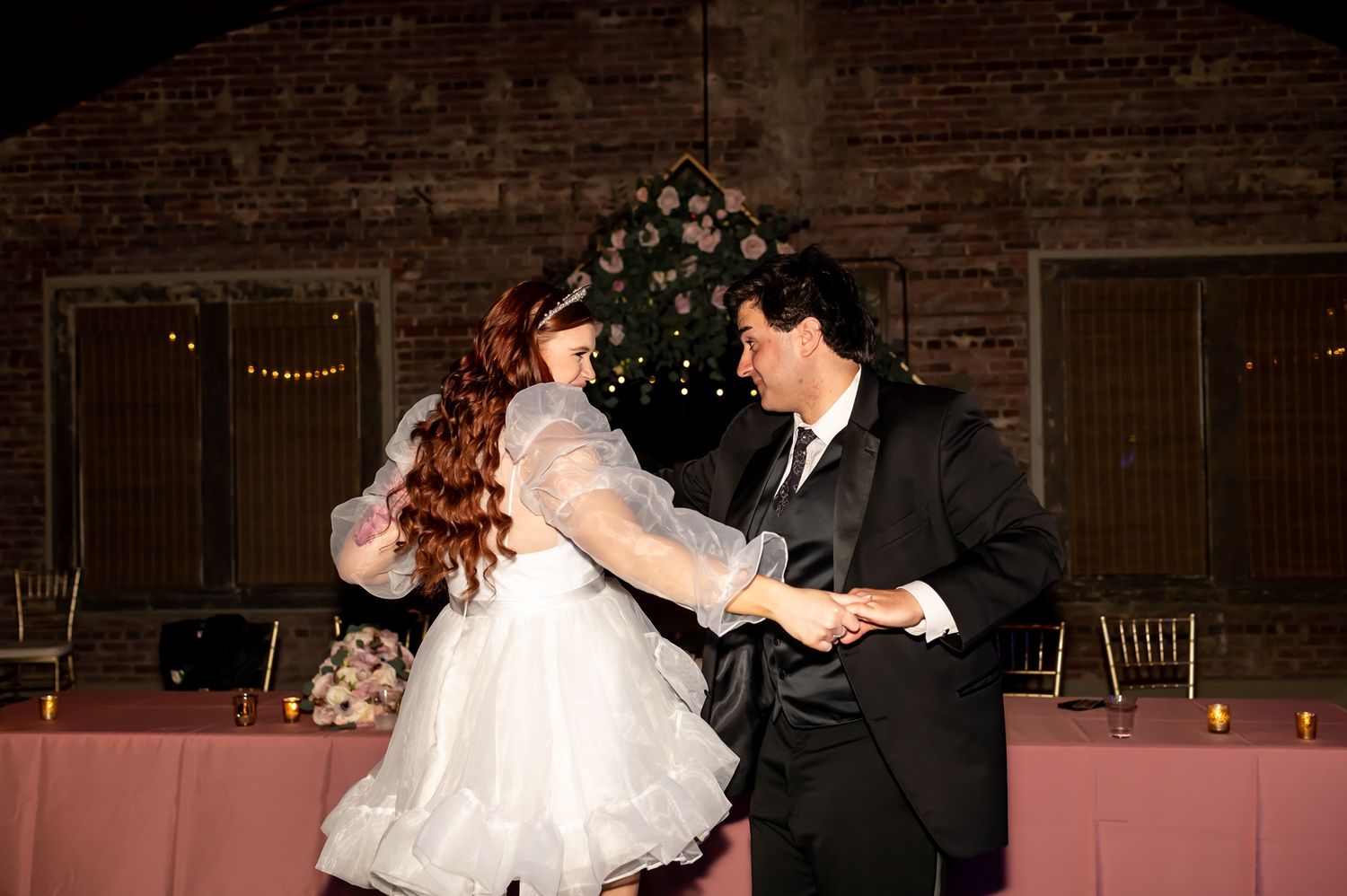 A couple at their wedding reception share an intimate dance in a rustic barn venue with dark wood walls.