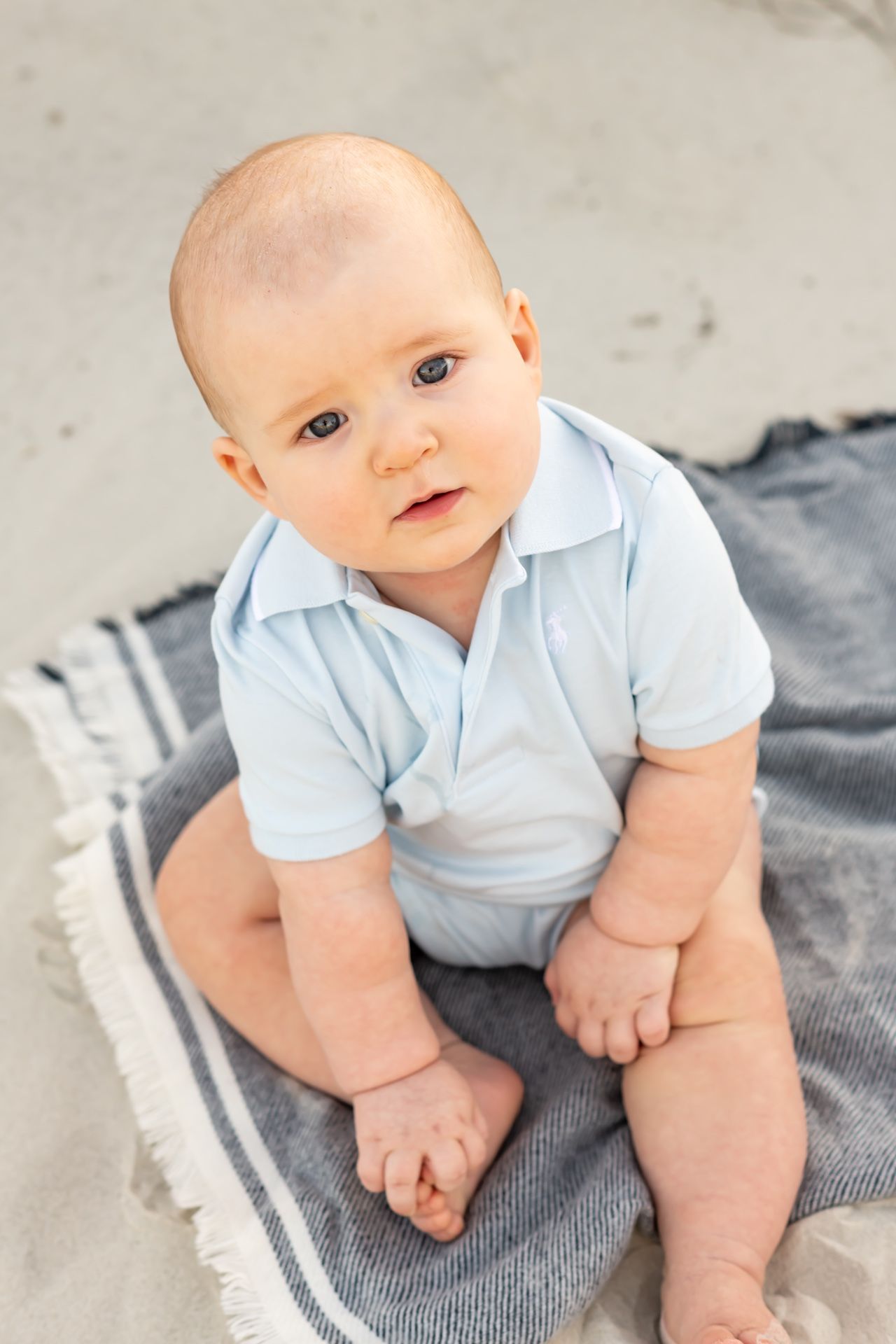 Baby wearing light blue polo onesie sits on gray blanket while displaying various expressions and poses.