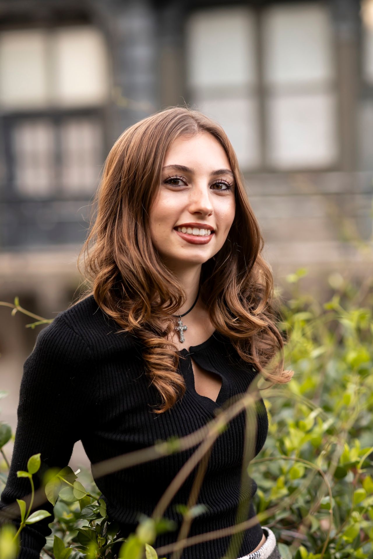 Portrait of person in black ribbed top standing near green foliage and plants outdoors in soft natural lighting.