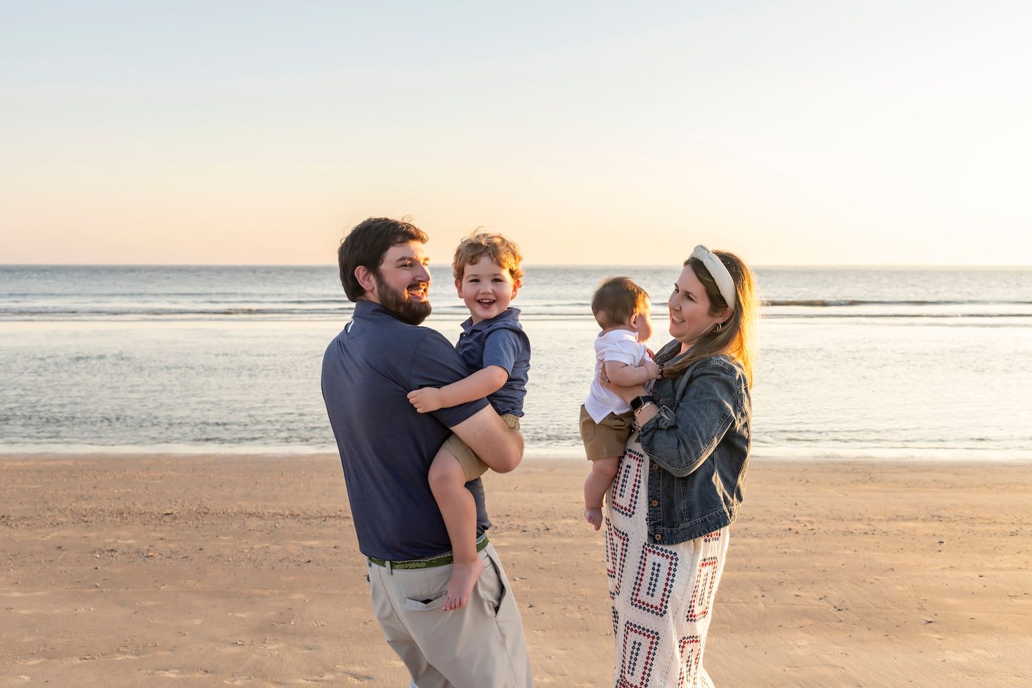 A happy family enjoying quality time together while standing on a scenic beach at sunset.