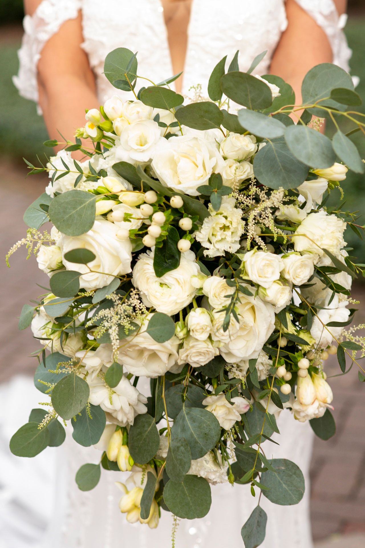 Close-up view of an elegant white bridal bouquet with roses and eucalyptus leaves arranged in a classic style.