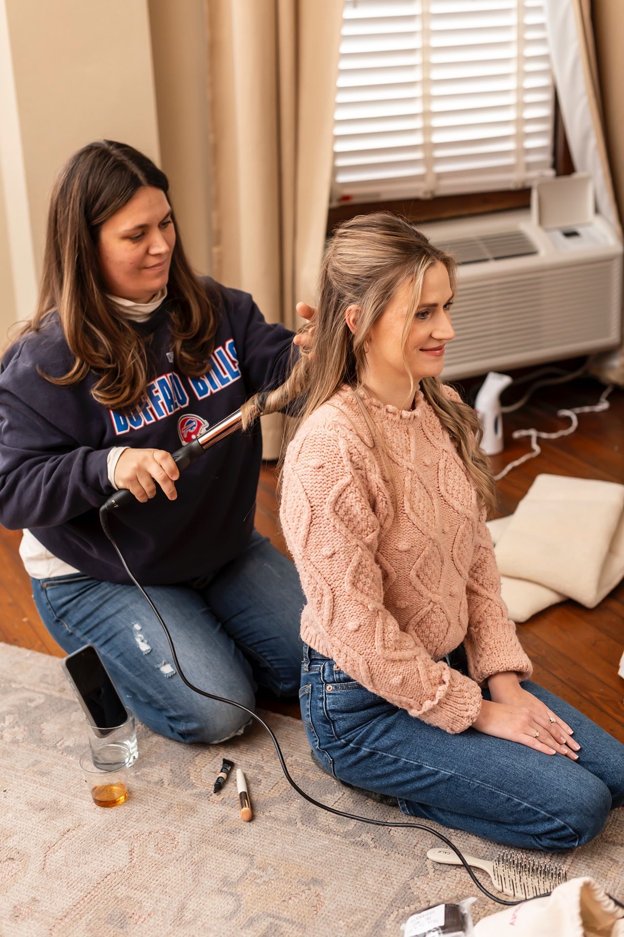 Two people sit on a hardwood floor working together on something while wearing casual clothing.