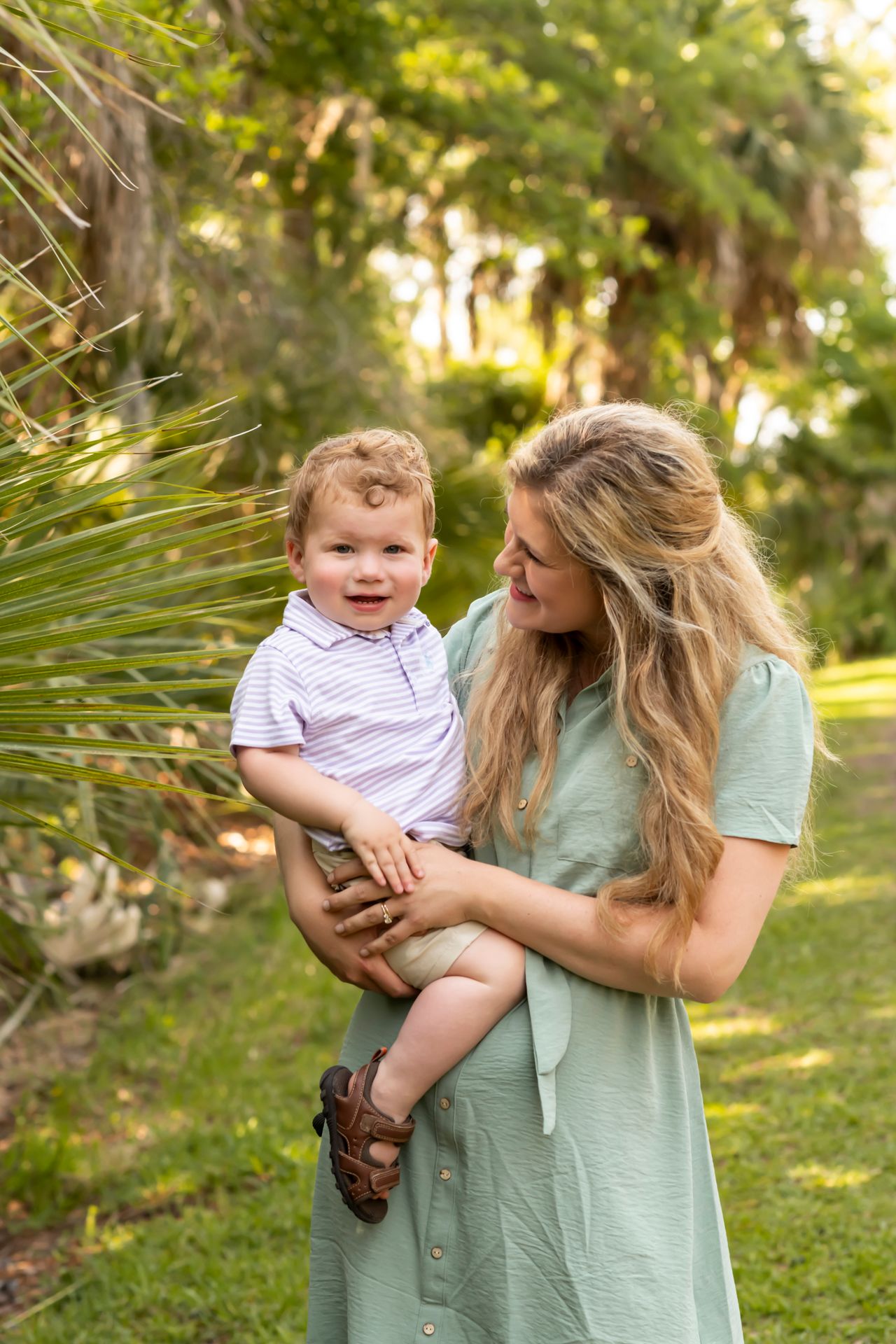 A parent and child share joyful moments together outdoors in a sunlit garden setting wearing mint green and white.