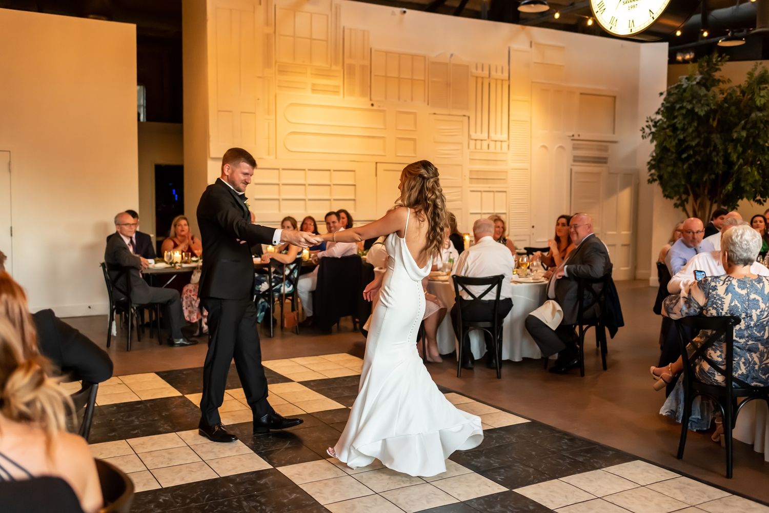 A couple celebrates their first dance at an indoor wedding reception with guests watching from banquet tables.