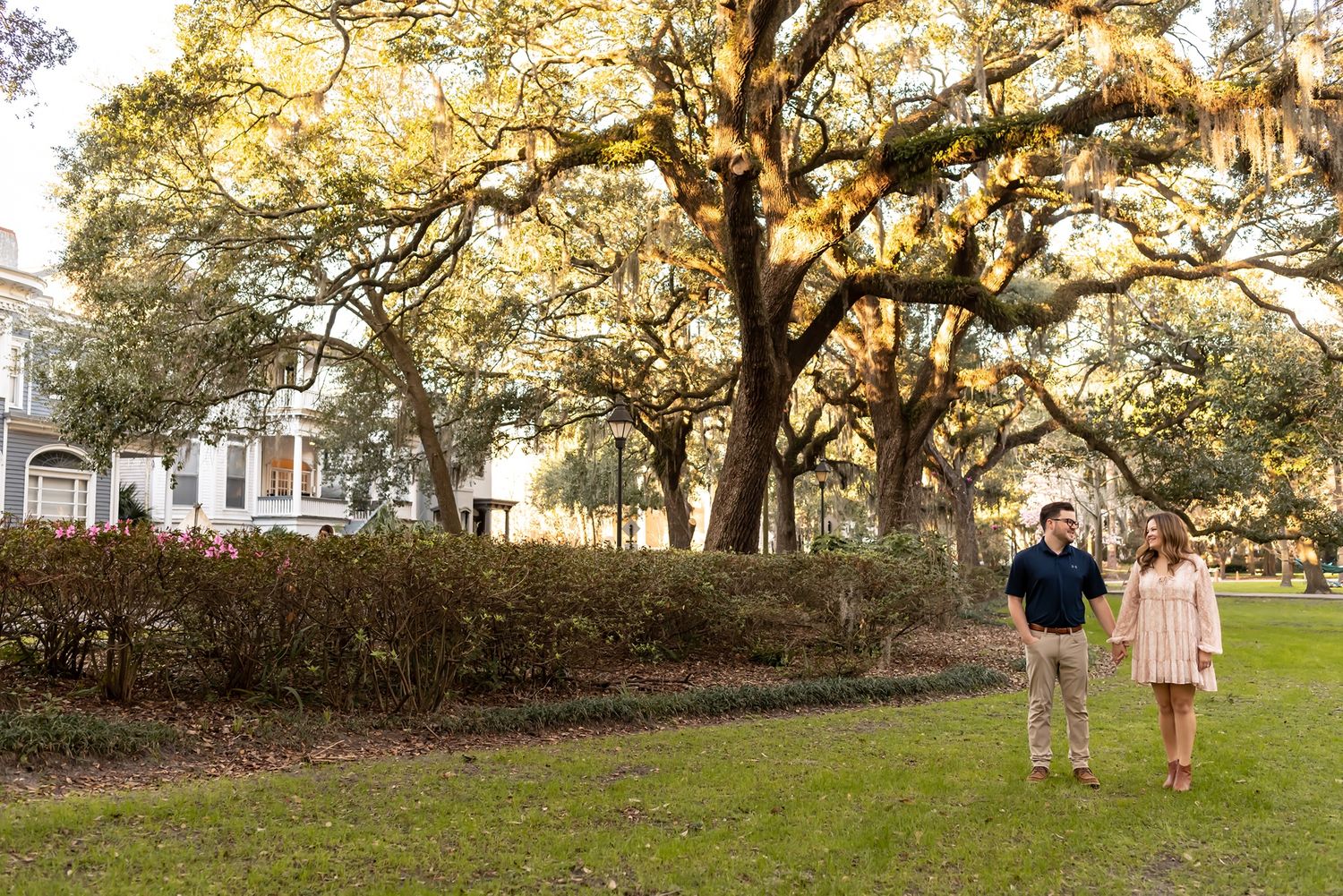 A happy couple walks together under golden sunlit trees during a romantic autumn photoshoot at sunset.