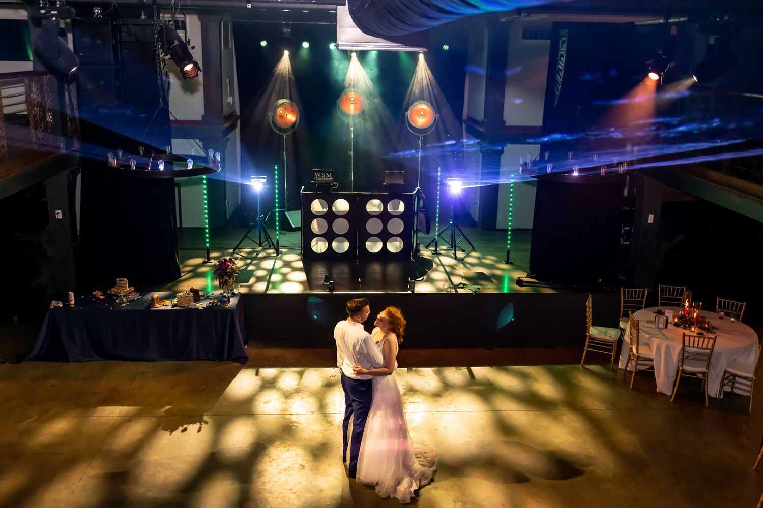 Couple dancing in an elegant music venue with dramatic stage lighting and empty tables at night.