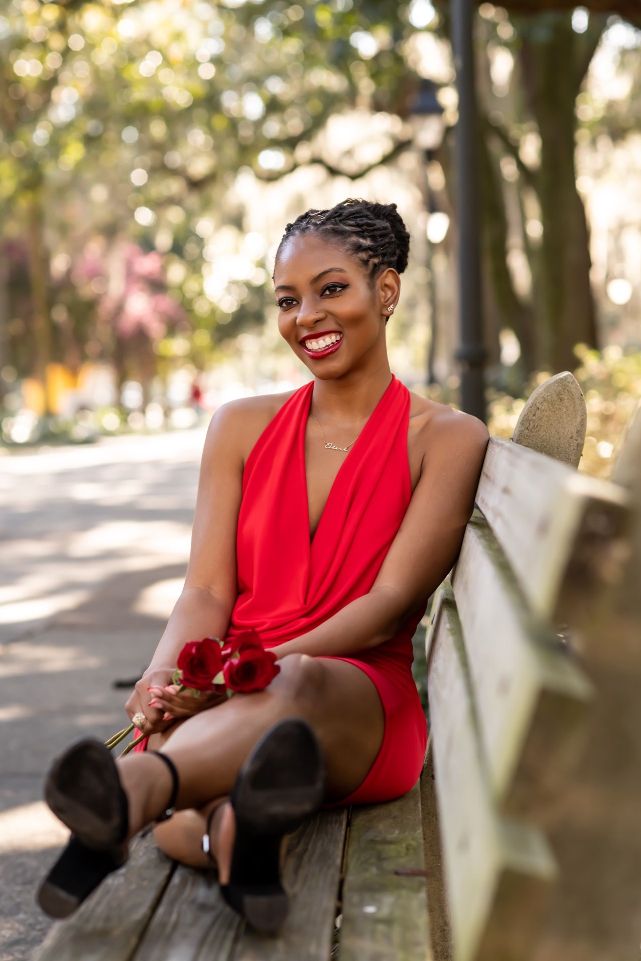A person in a striking red halter dress sits on a park bench on a sunny autumn day with blurred trees in background.