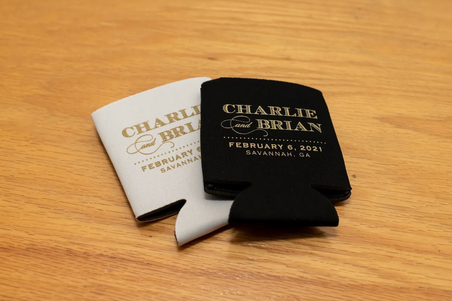 Two custom drink koozies in black and white colors with text displayed on wooden surface.