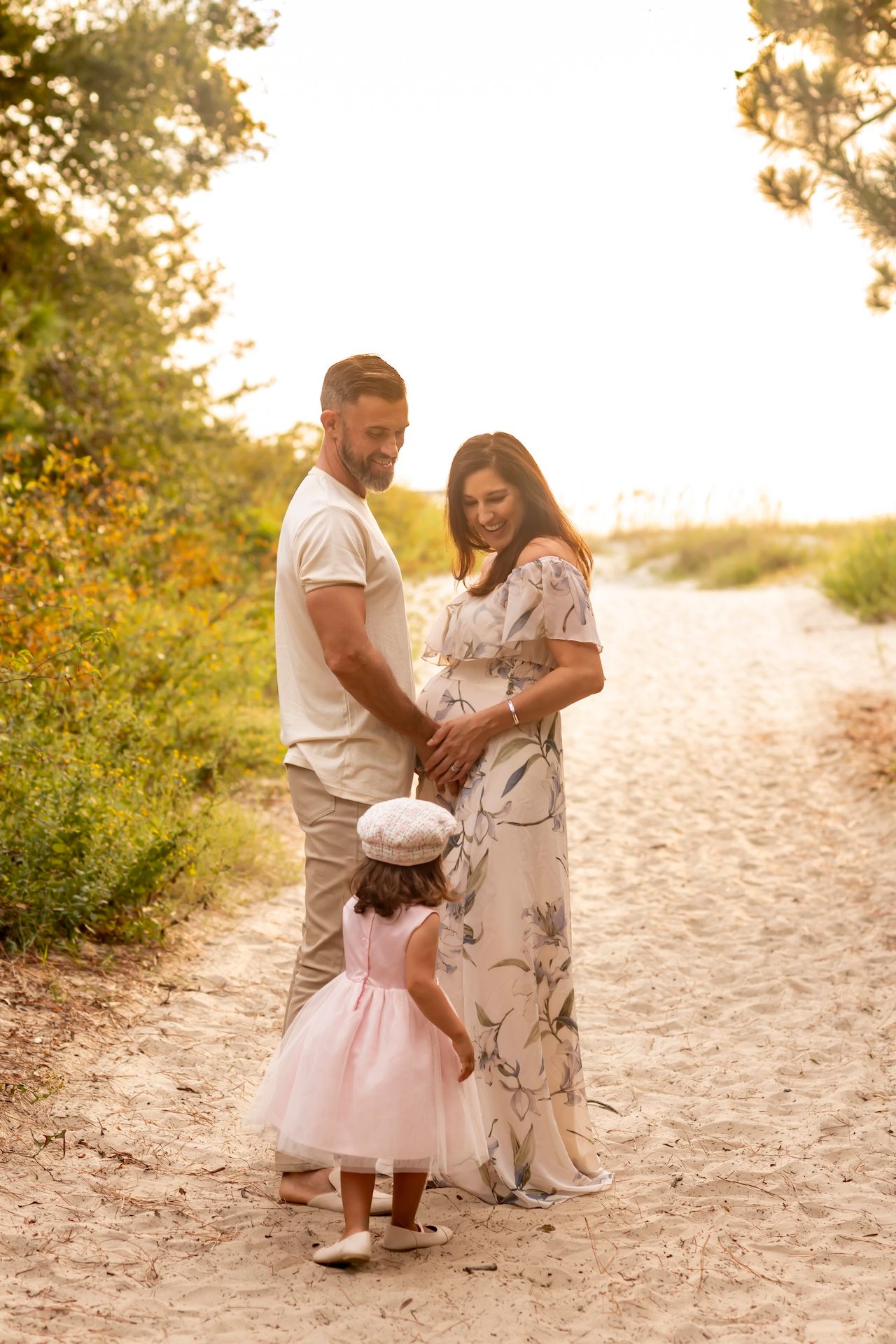 A couple in light colored outfits embracing on a sandy beach path during golden hour sunset.